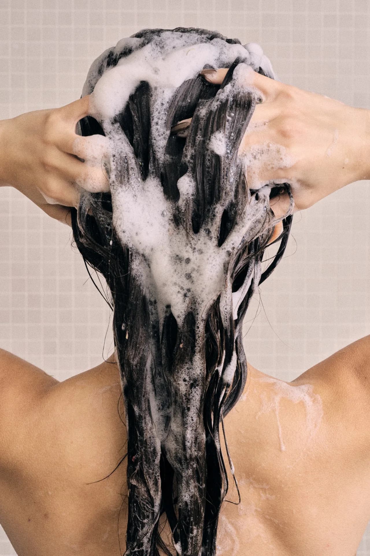 Woman washing her hair with foam, seen from behind